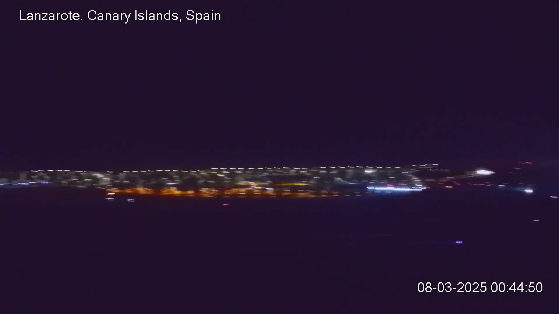 A long, blurred line of city lights is visible at night under a dark sky.