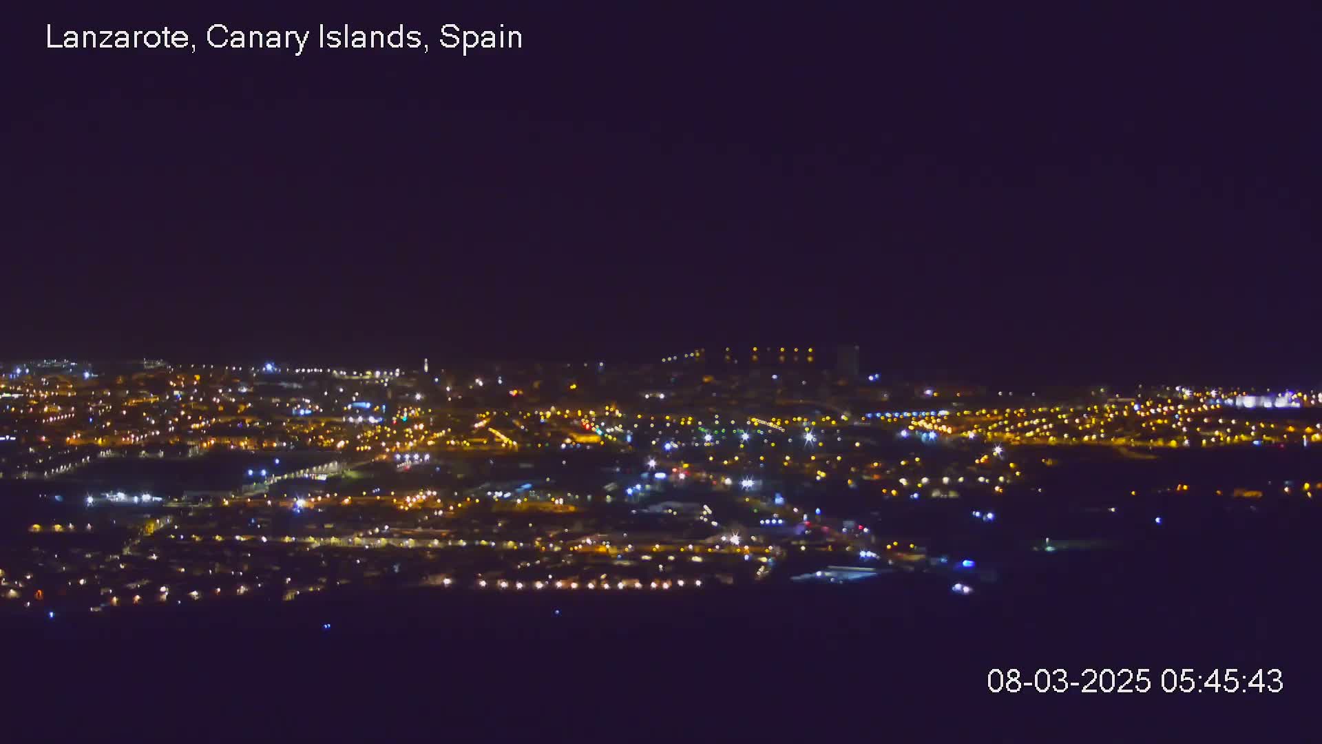 A nighttime, aerial view shows a sprawling city illuminated by countless small lights under a clear, dark sky.