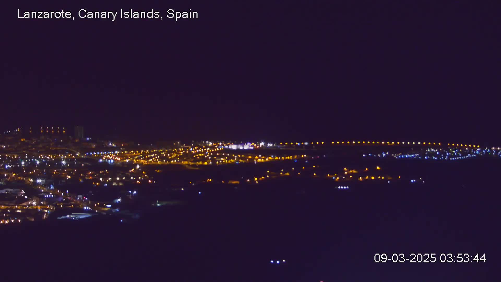 A nighttime view of a city illuminated by numerous lights under a clear, dark sky.