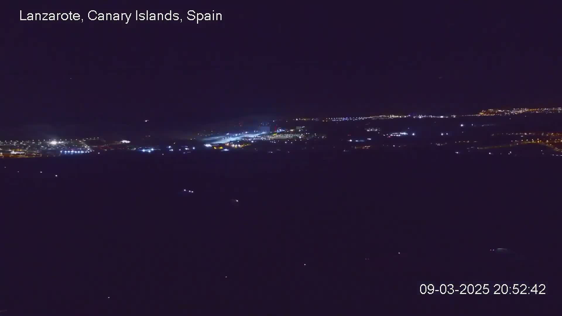 A nighttime, long-range view shows a distant city illuminated with scattered lights under a clear, dark sky.
