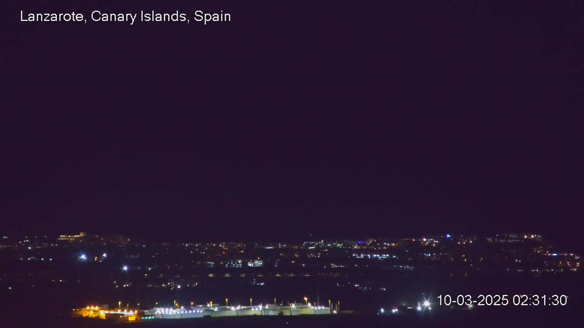 A nighttime view of a city illuminated by many scattered lights under a clear, dark sky.