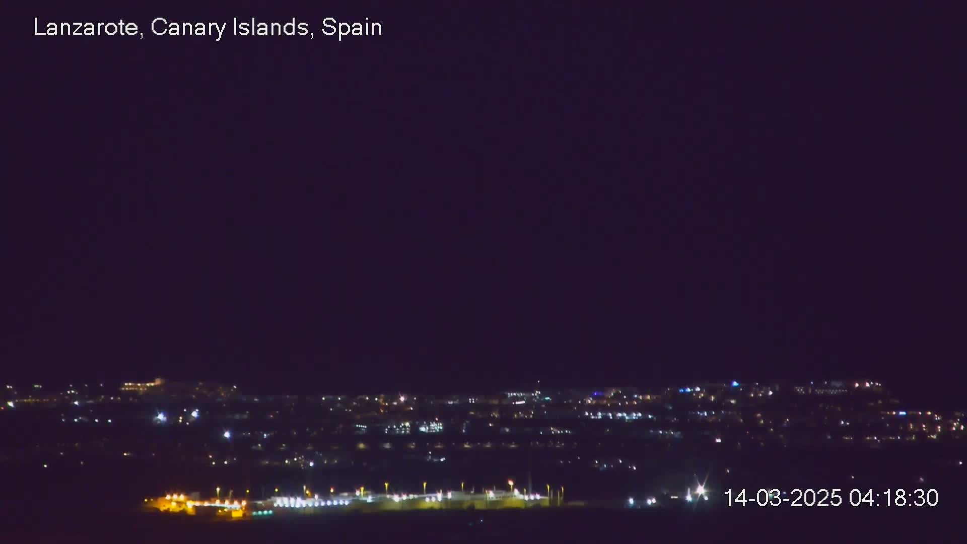 A nighttime long shot shows a city illuminated by many small, scattered lights under a clear, dark sky.