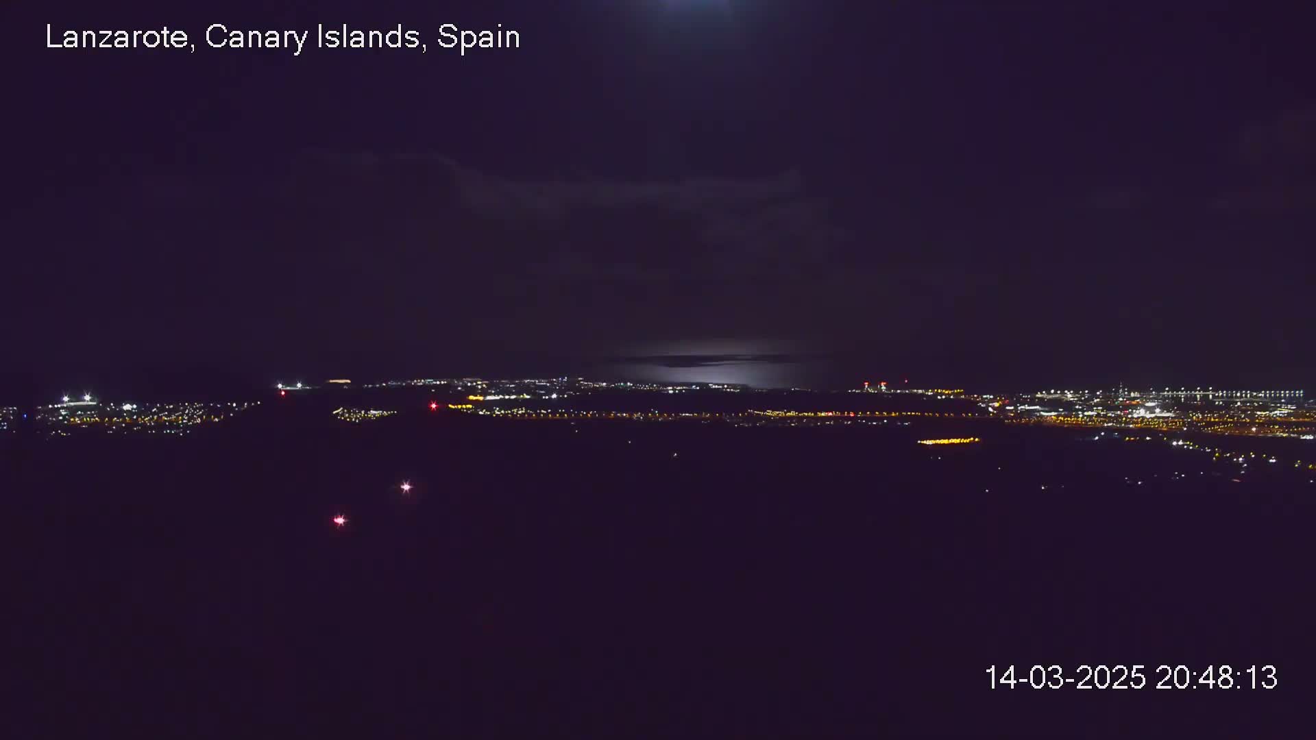 A nighttime long shot shows a city glowing with lights under a partly cloudy sky.