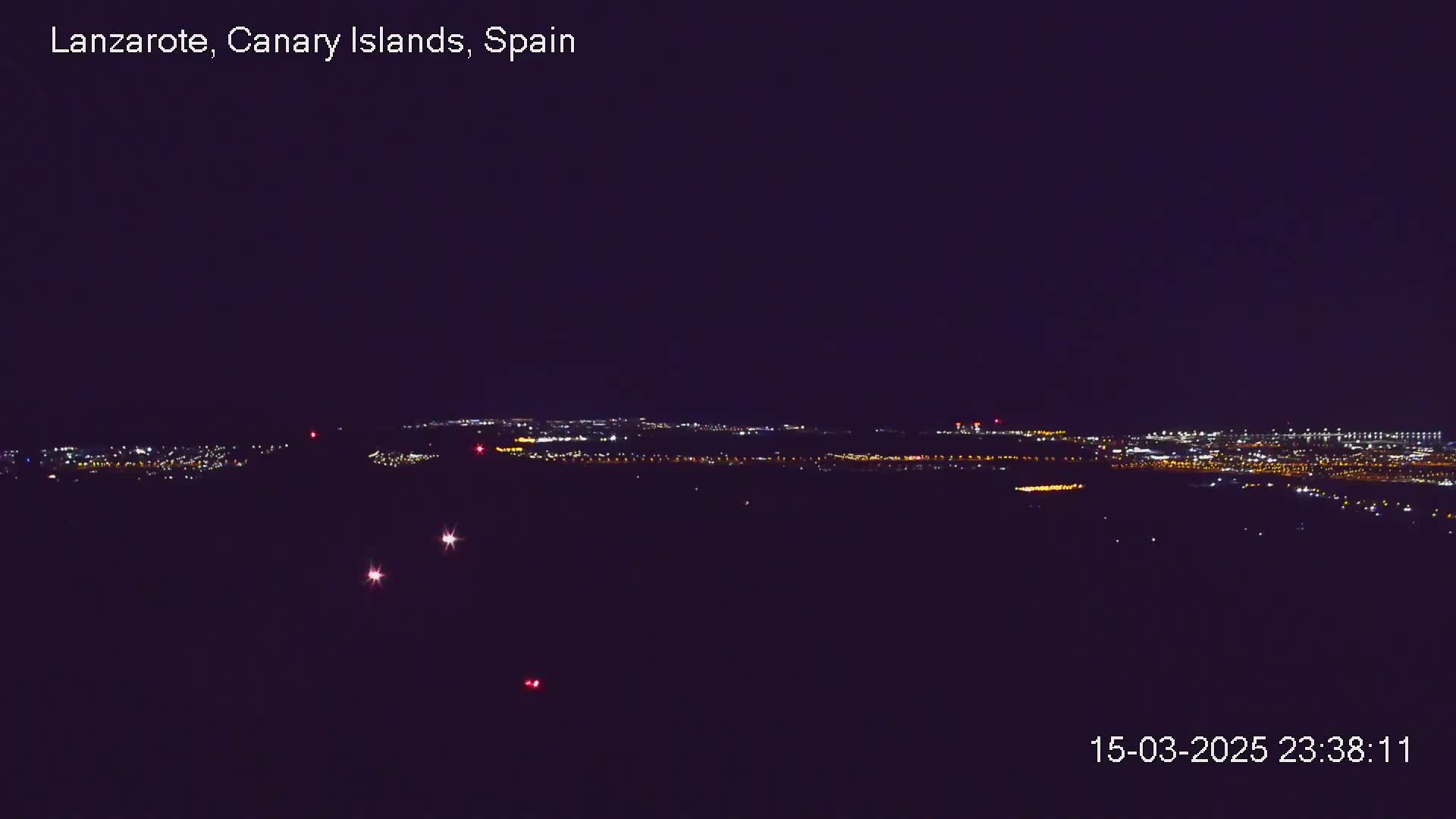 A nighttime long shot reveals a distant city illuminated by numerous lights under a dark, clear sky.