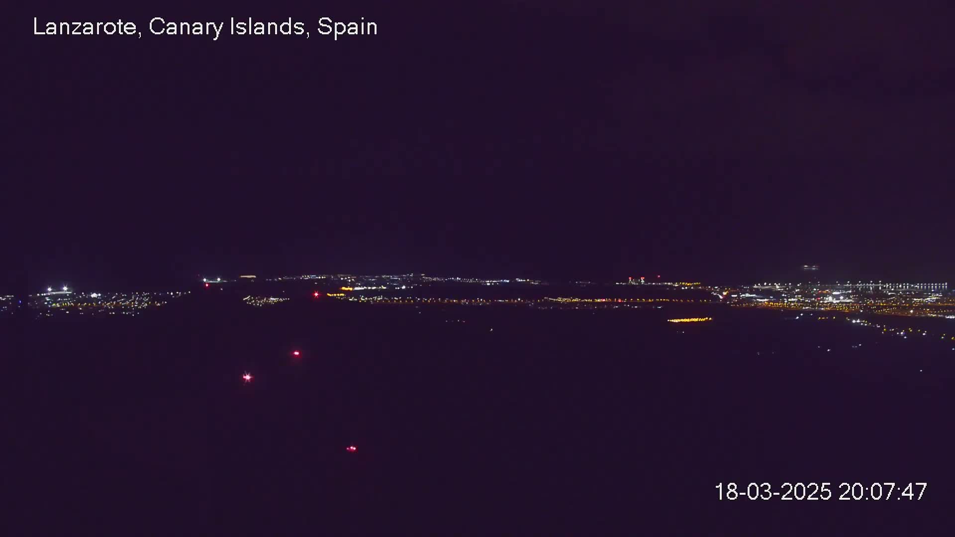 A nighttime view shows a distant city illuminated with many lights under a dark sky.