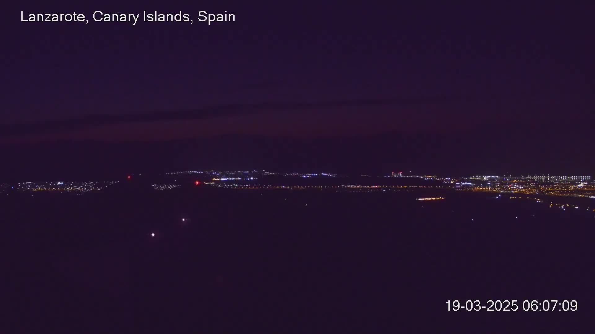 A nighttime, long-range view of a city illuminated by lights under a dark, mostly clear sky.