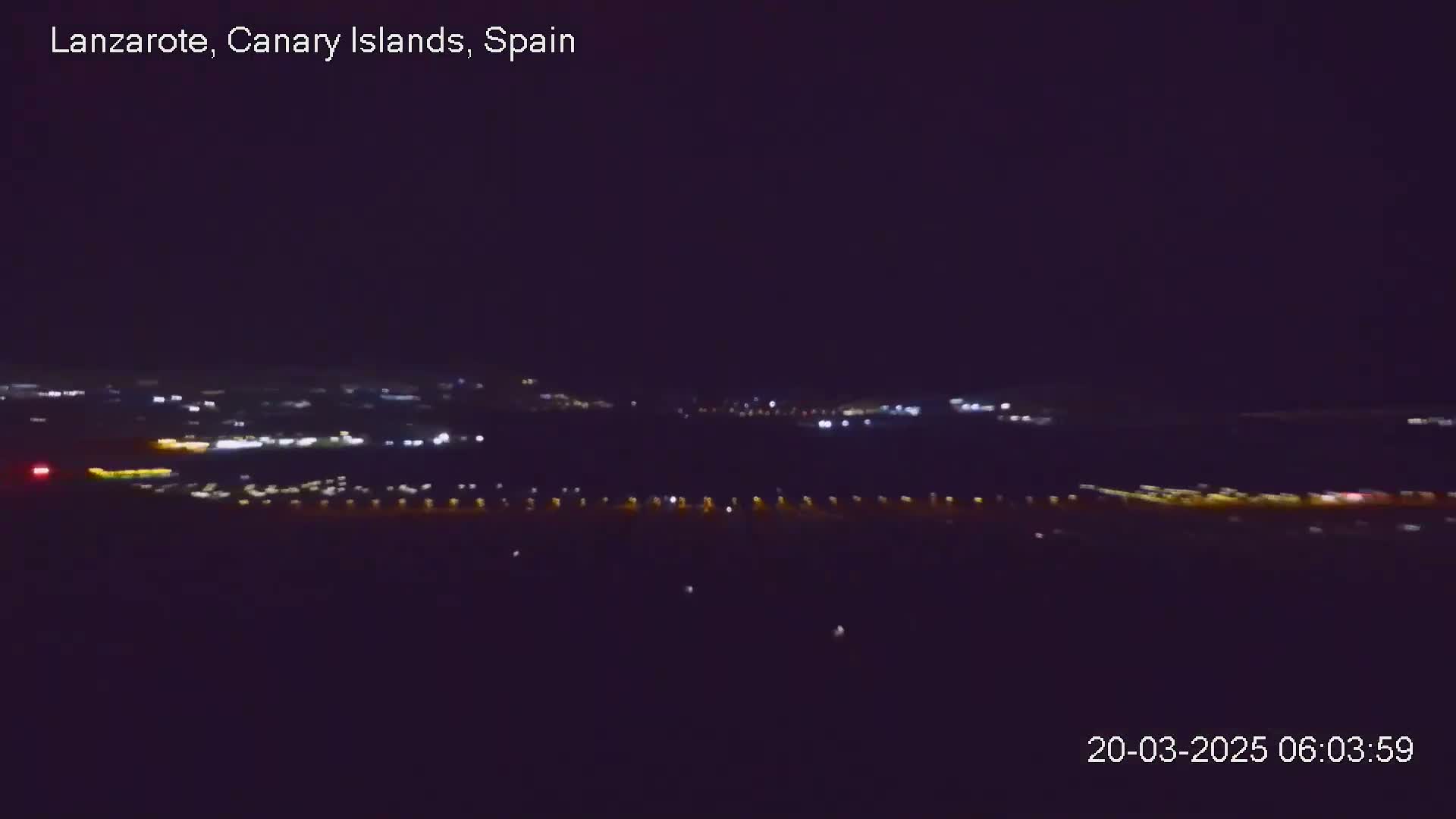 A nighttime long shot of a city's lights spread across a dark landscape under a clear sky.