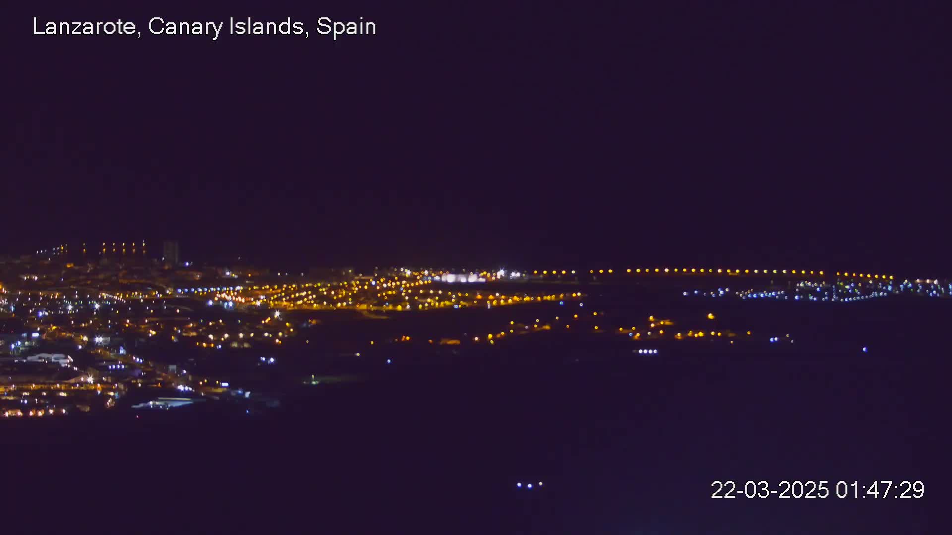 A nighttime long shot shows a sprawling city illuminated by numerous lights under a clear, dark sky.