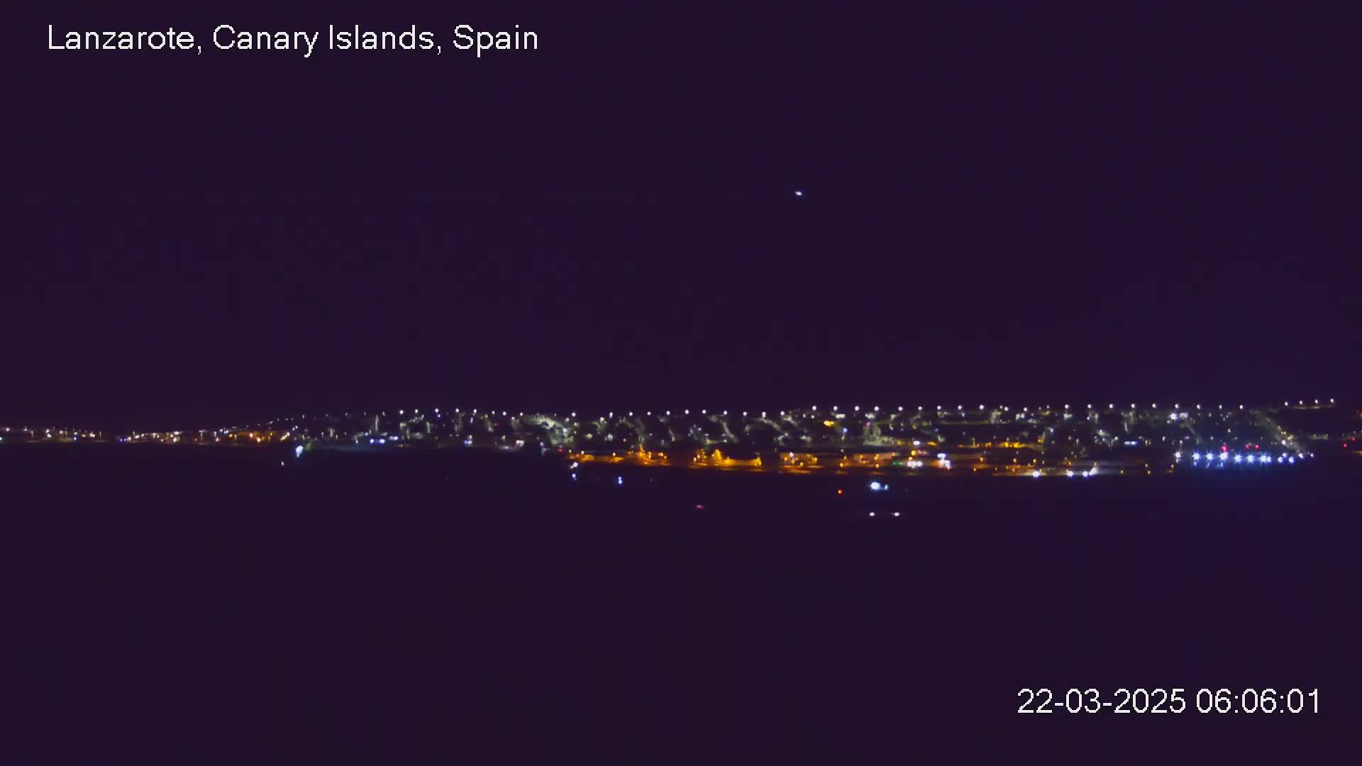 A nighttime long shot shows a line of city lights against a dark, clear sky.