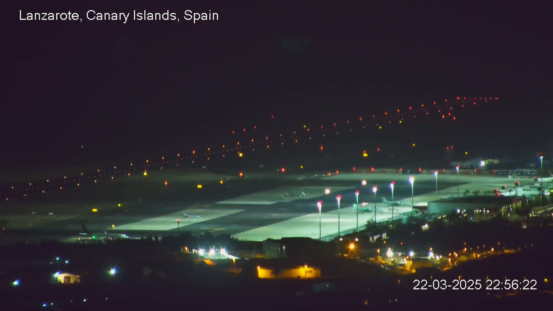 A brightly lit airport runway and surrounding buildings are visible at night.