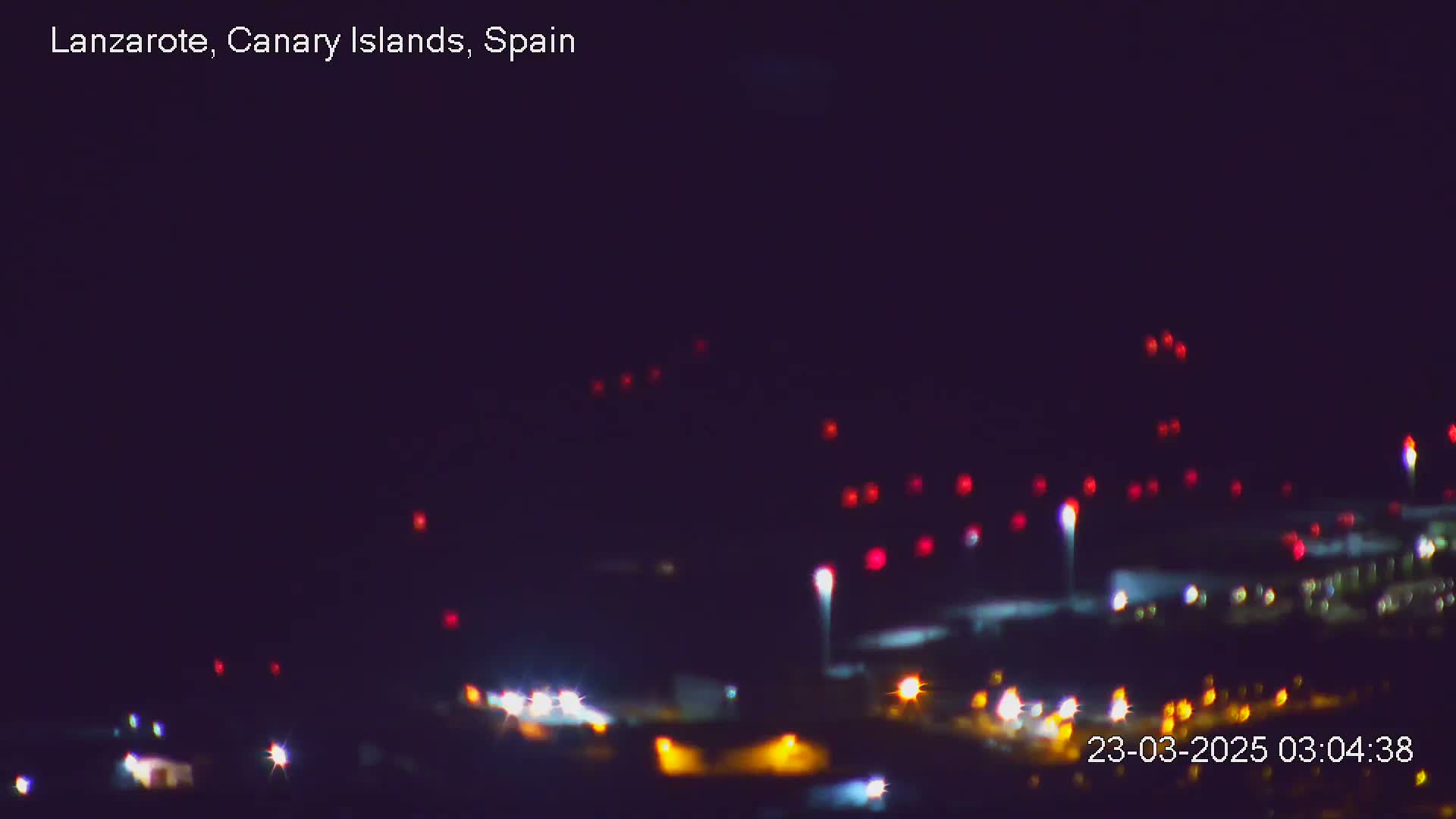 A blurry nighttime view of an airfield with numerous red and white lights visible in the dark sky.