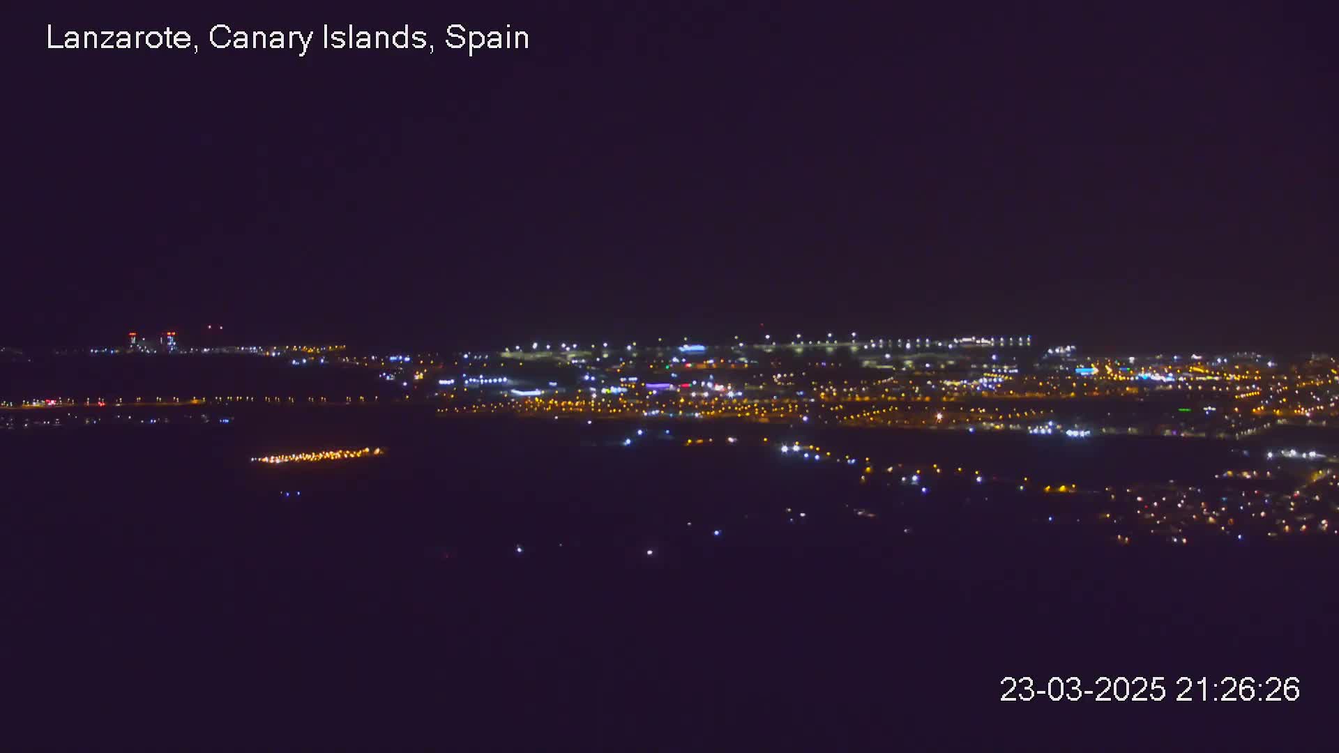 A nighttime long shot of a city illuminated by many lights under a clear, dark sky.