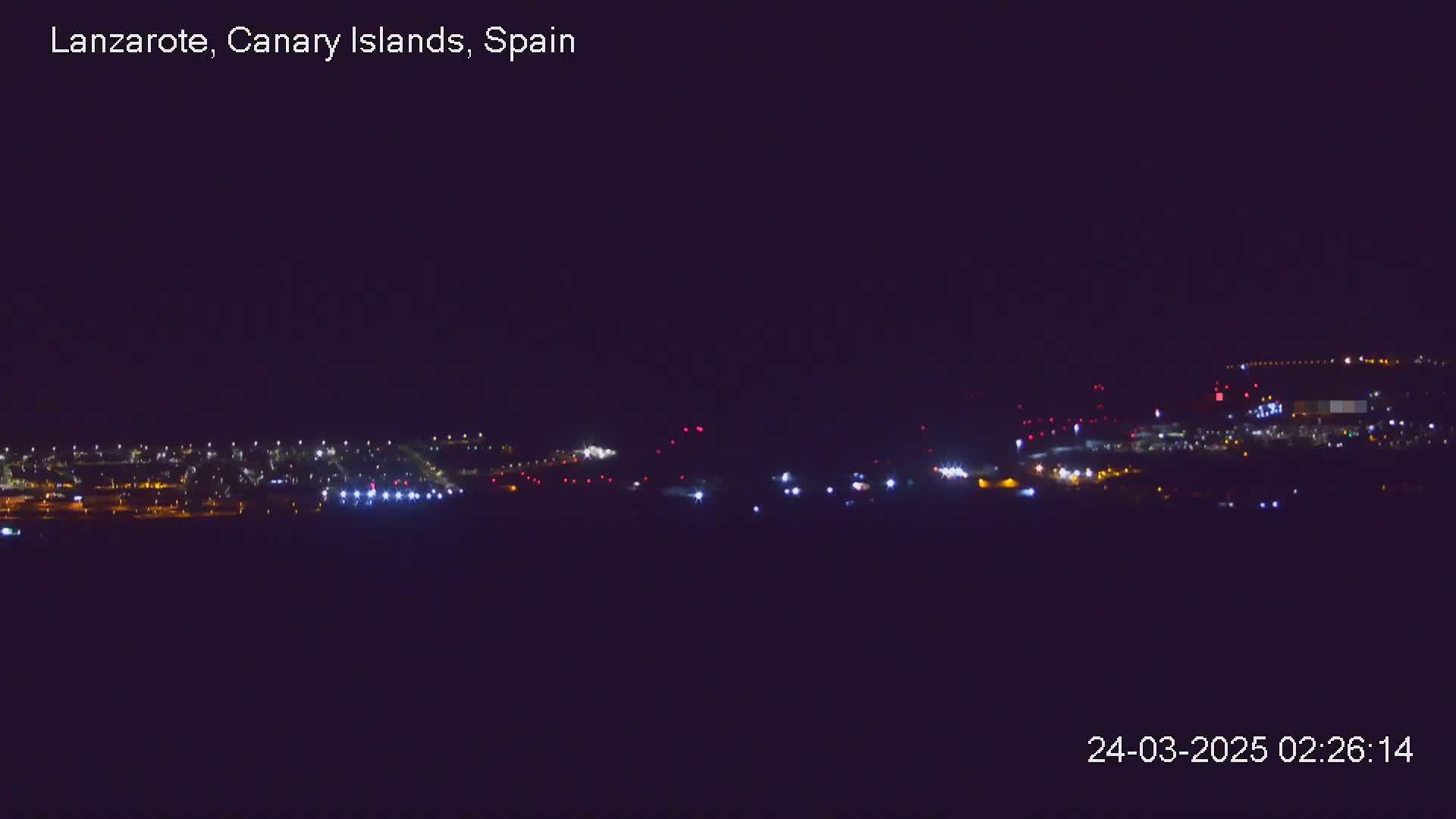 A nighttime long shot shows a city illuminated by many lights under a dark, clear sky.