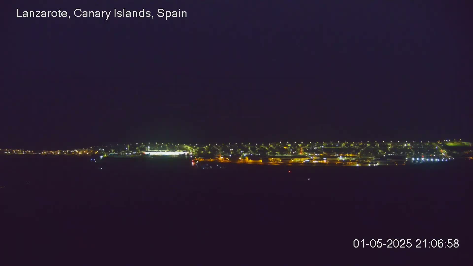A nighttime long shot shows a line of lights from a town or city under a dark, clear sky.