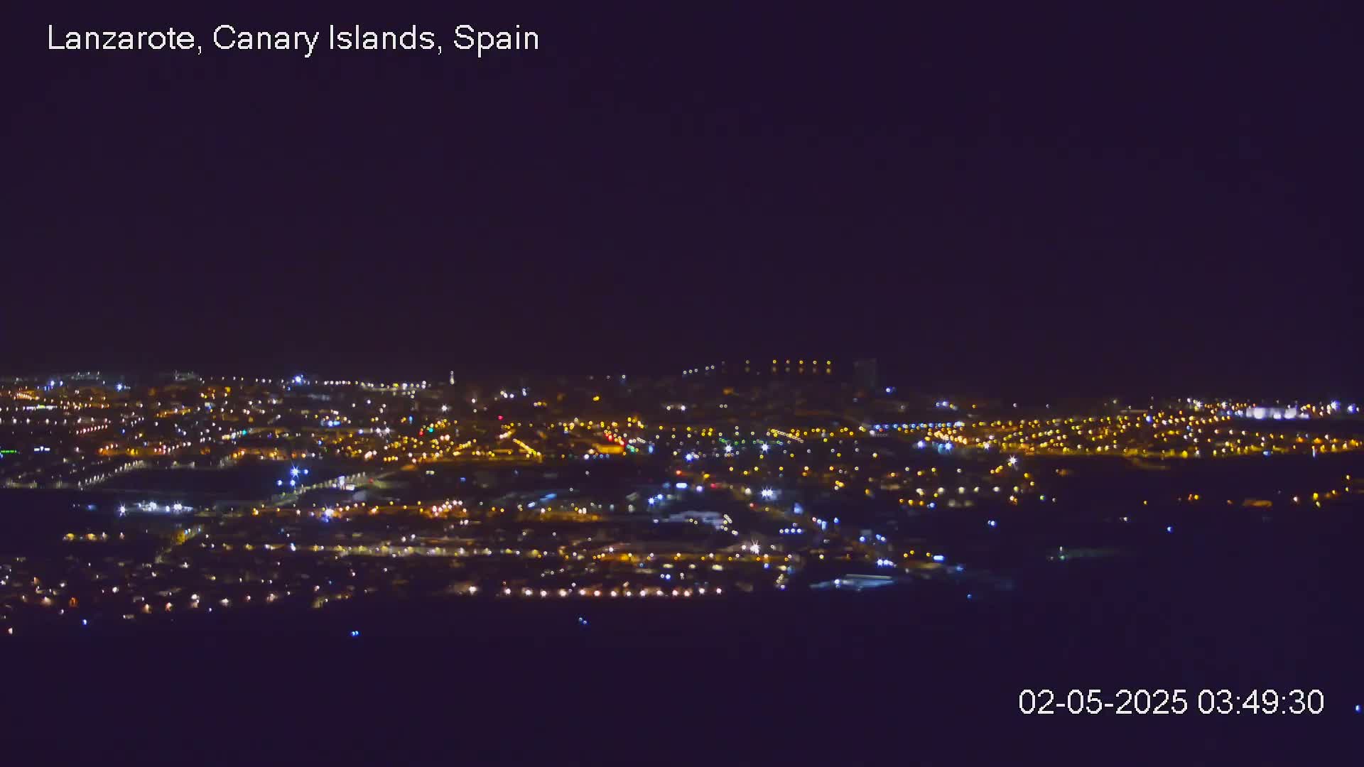 A nighttime aerial view of a city illuminated by countless lights under a clear, dark sky.