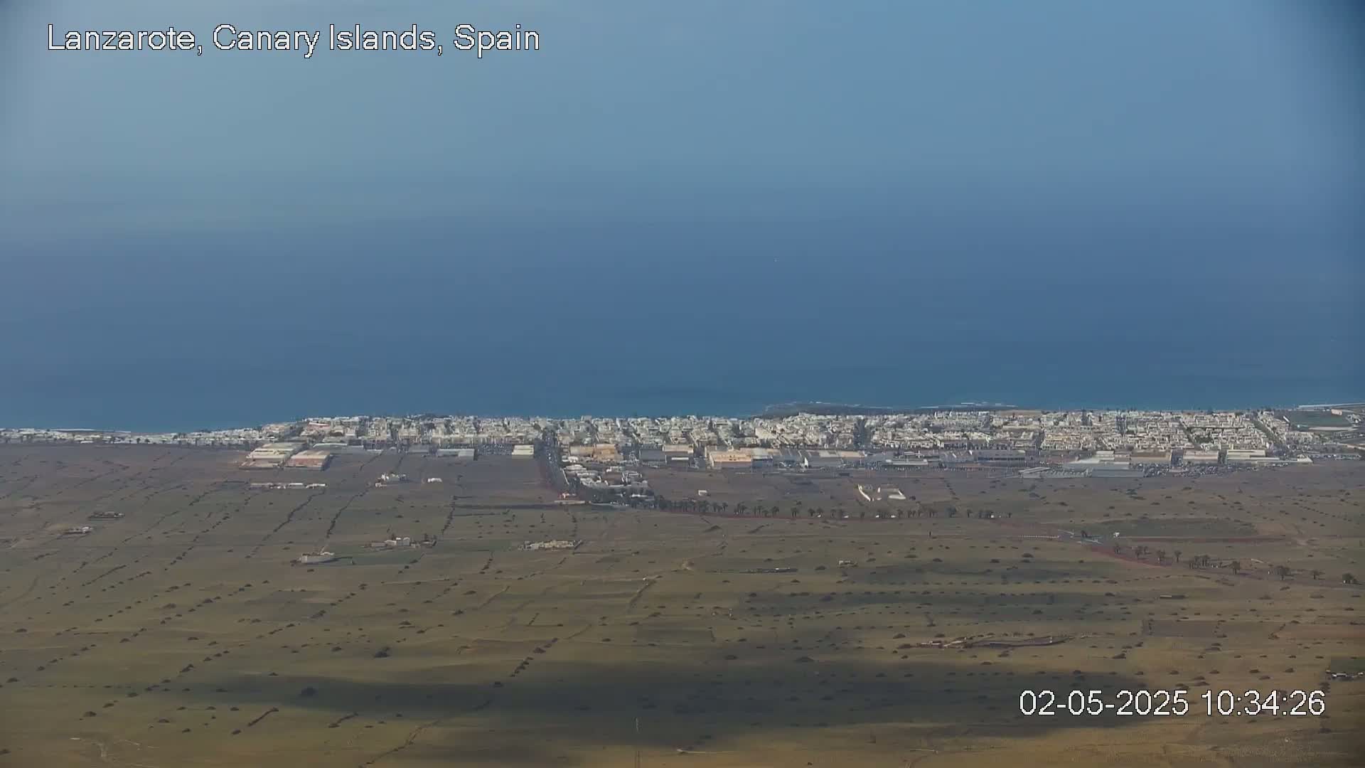 A coastal town with light-colored buildings stretches along the ocean under a clear, bright sky.