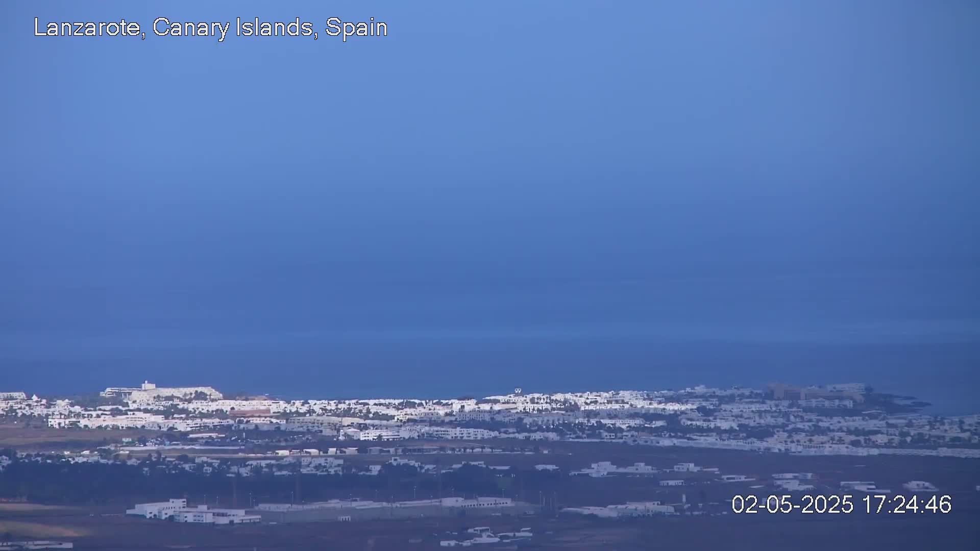A coastal town with white buildings stretches along the ocean under a clear blue sky.