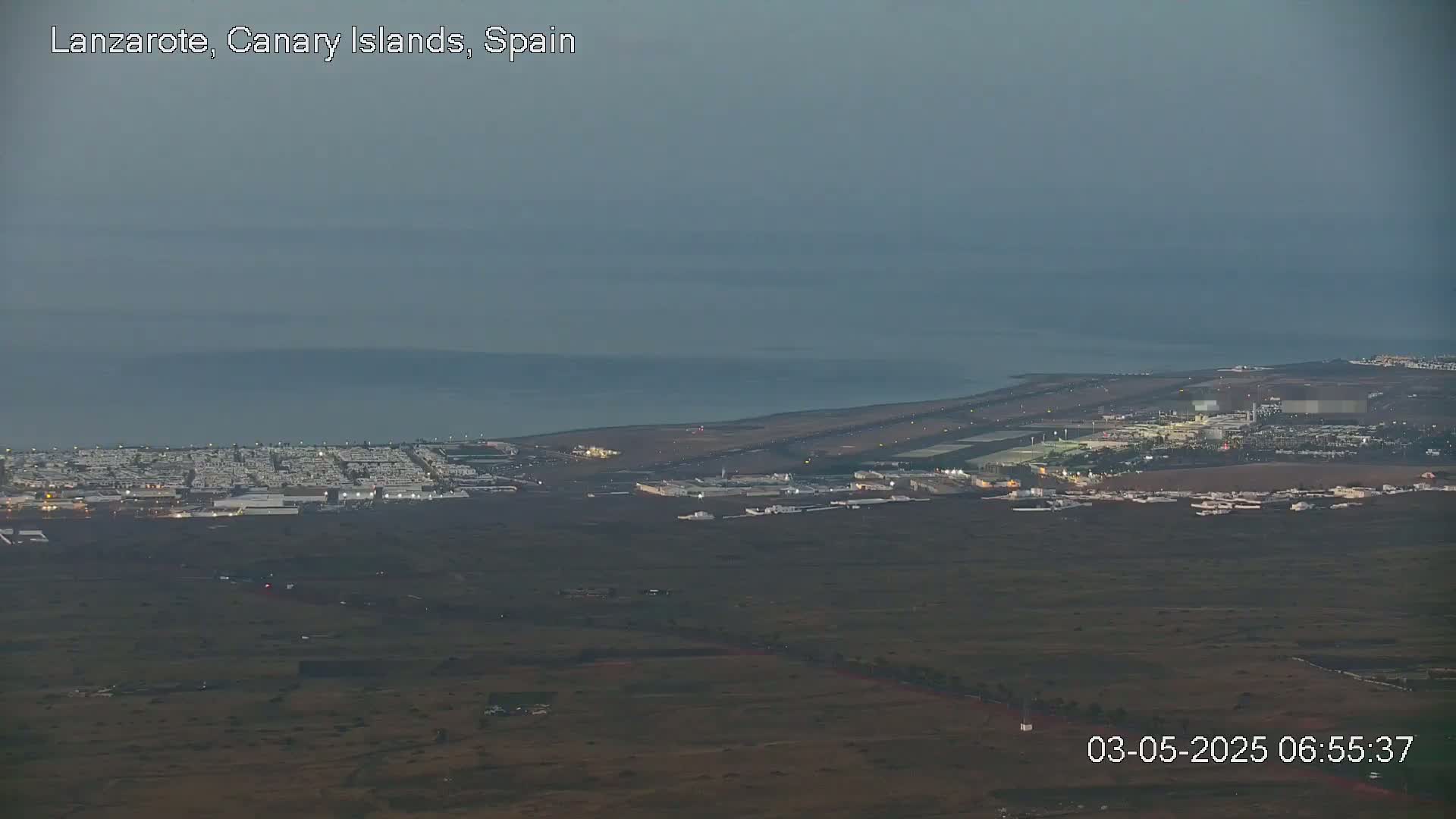 A coastal airport and surrounding buildings are visible under a dusky, overcast sky.