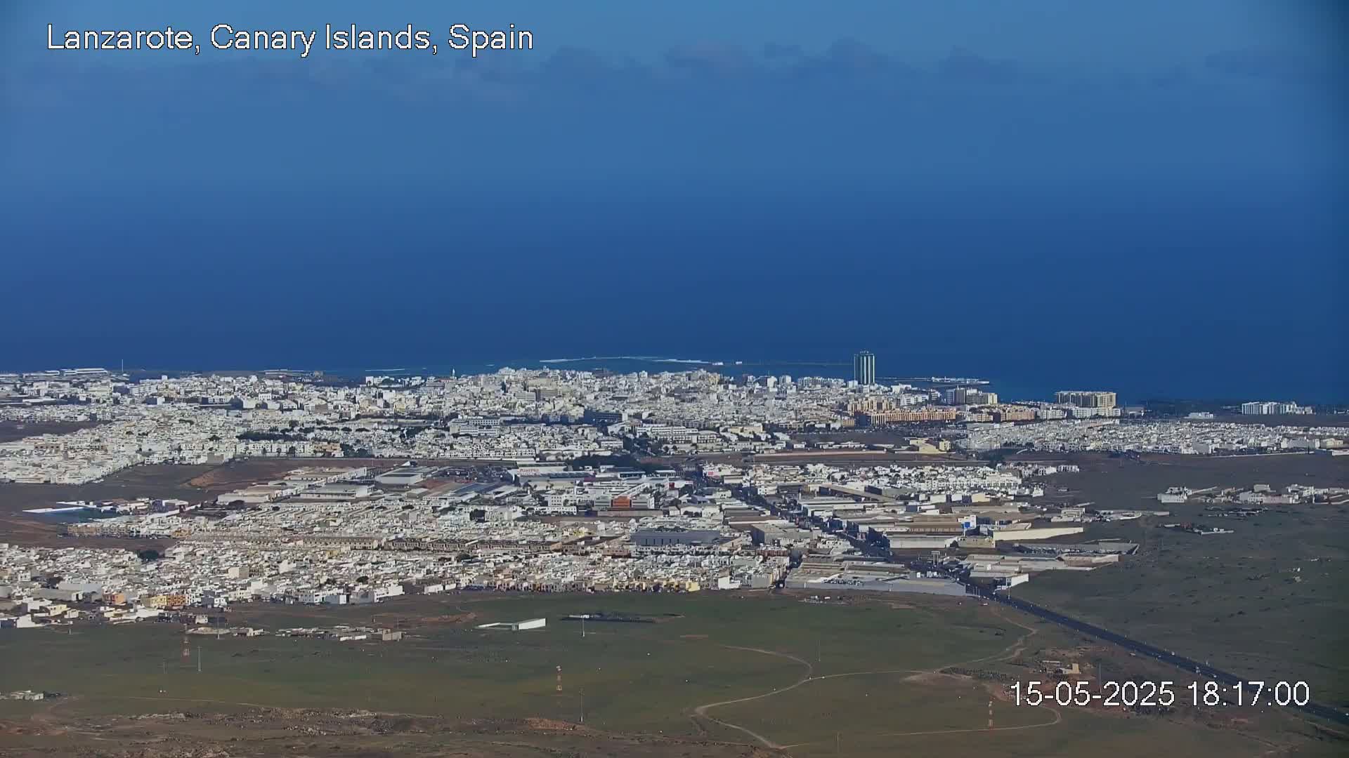 A sprawling city with light-colored buildings extends to a calm blue ocean under a clear sky.