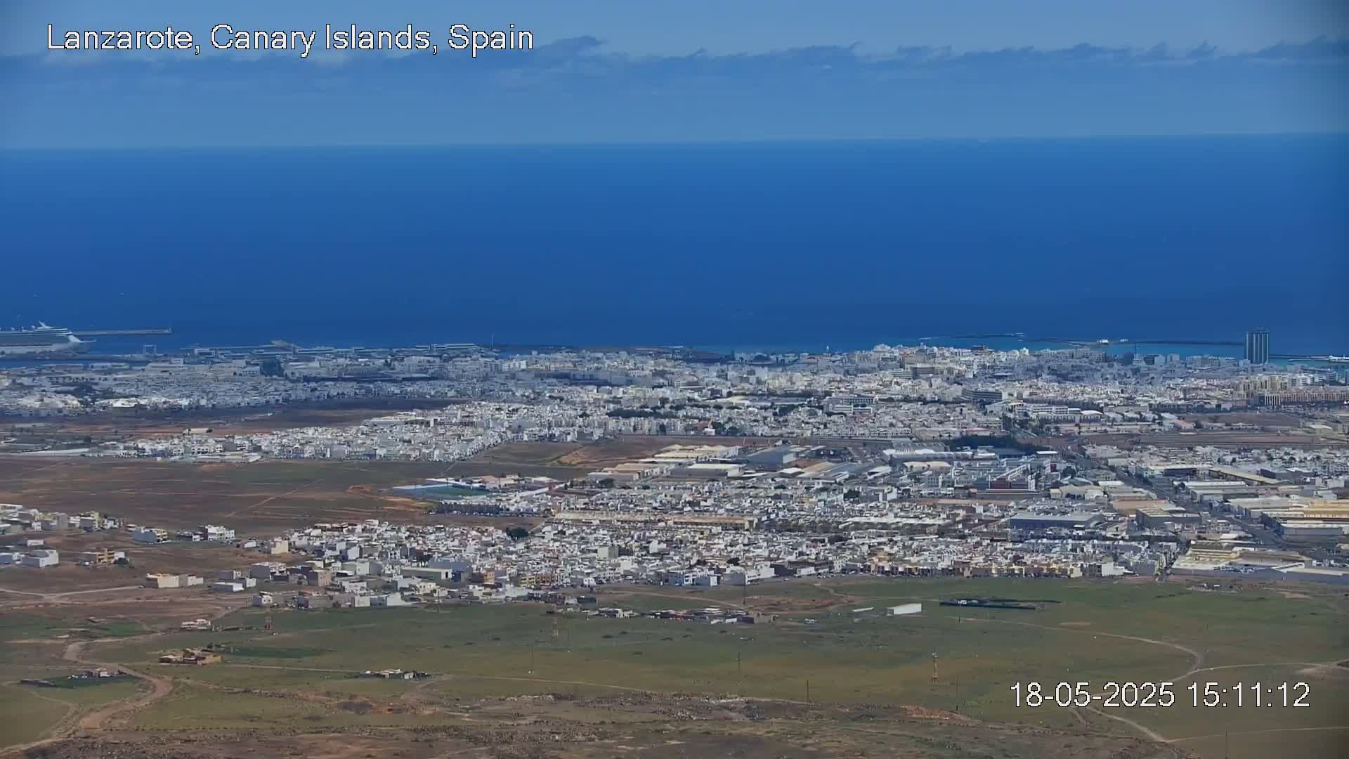 A sprawling coastal city with light-colored buildings extends to a vast blue ocean under a mostly clear sky.