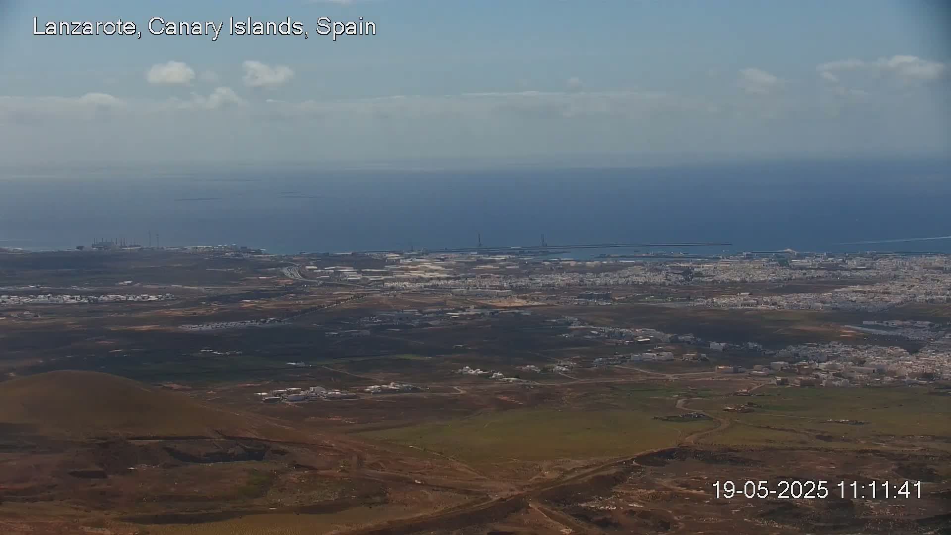 A high-angle view shows a coastal town and ocean under a mostly clear sky with a few scattered clouds.