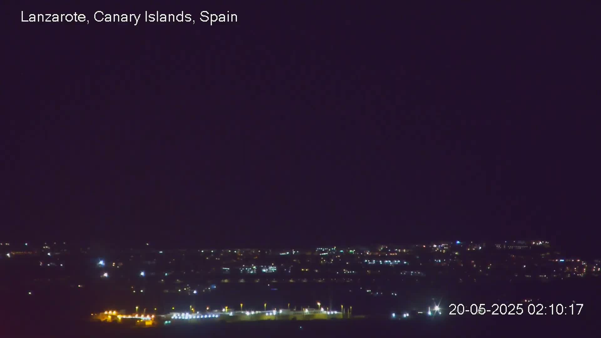 A nighttime long shot of a city illuminated by scattered lights under a clear, dark sky.