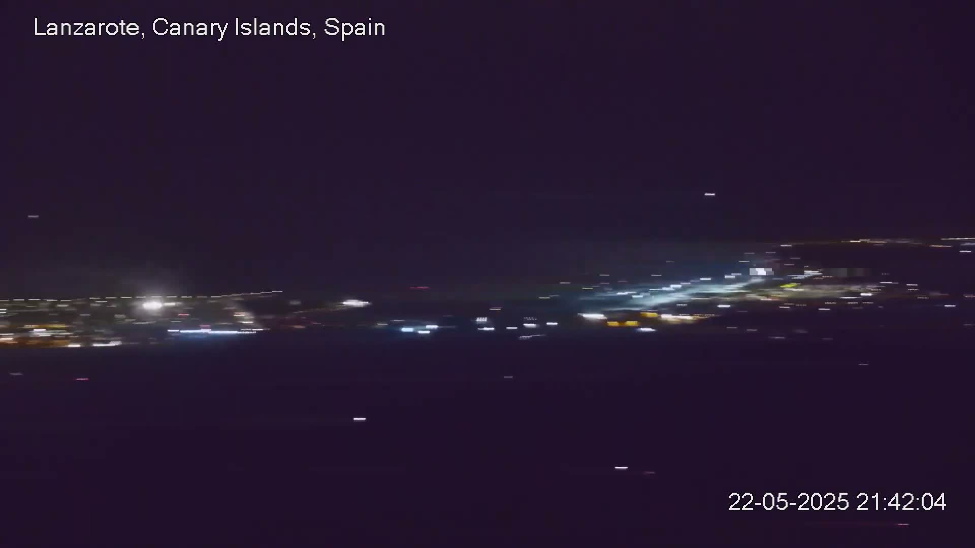 A nighttime long shot shows a blurry view of city lights spread across a dark landscape under a clear sky.