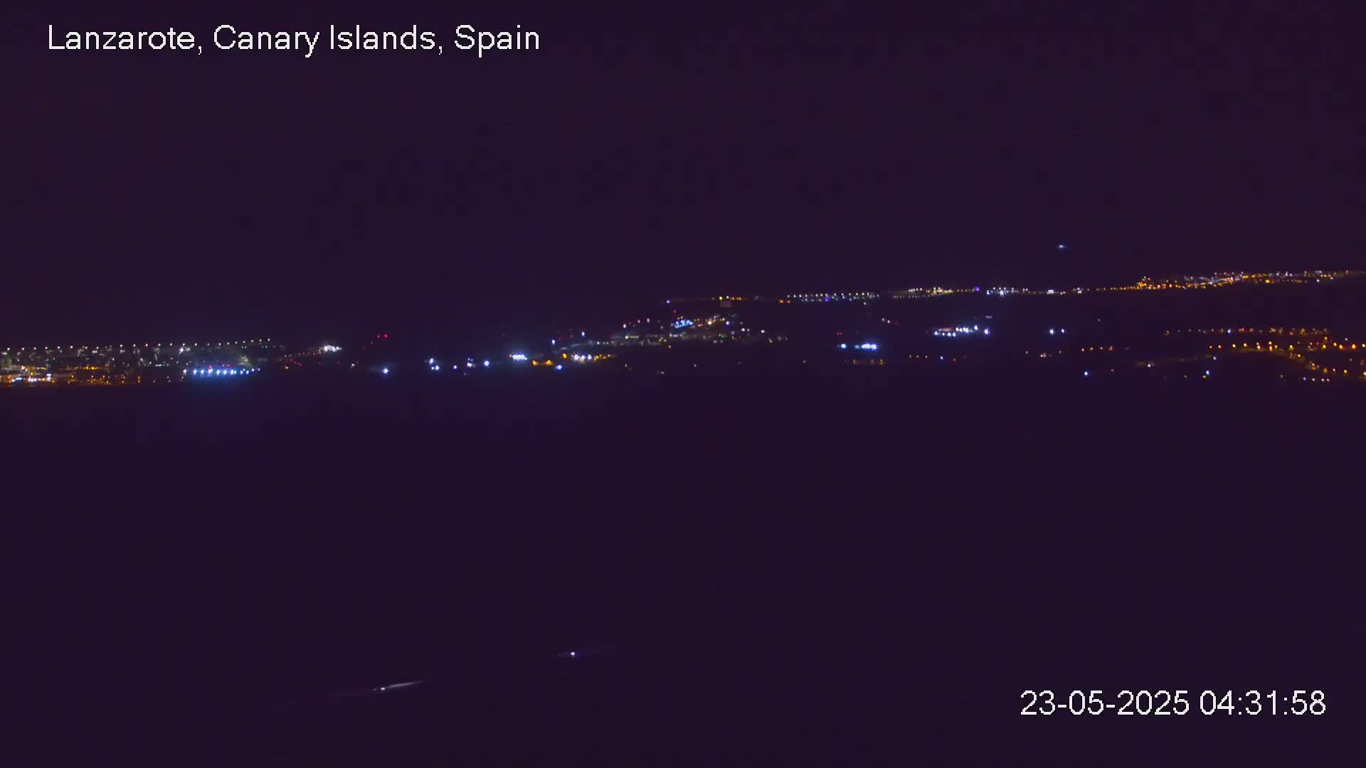 A distant, dimly lit town is visible at night under a dark sky.