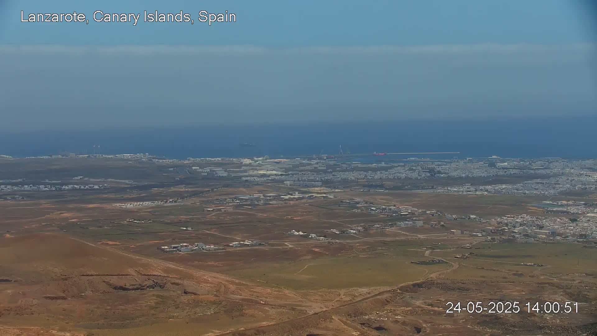 A high-angle view shows a coastal town with a hazy sky and calm ocean in the background.