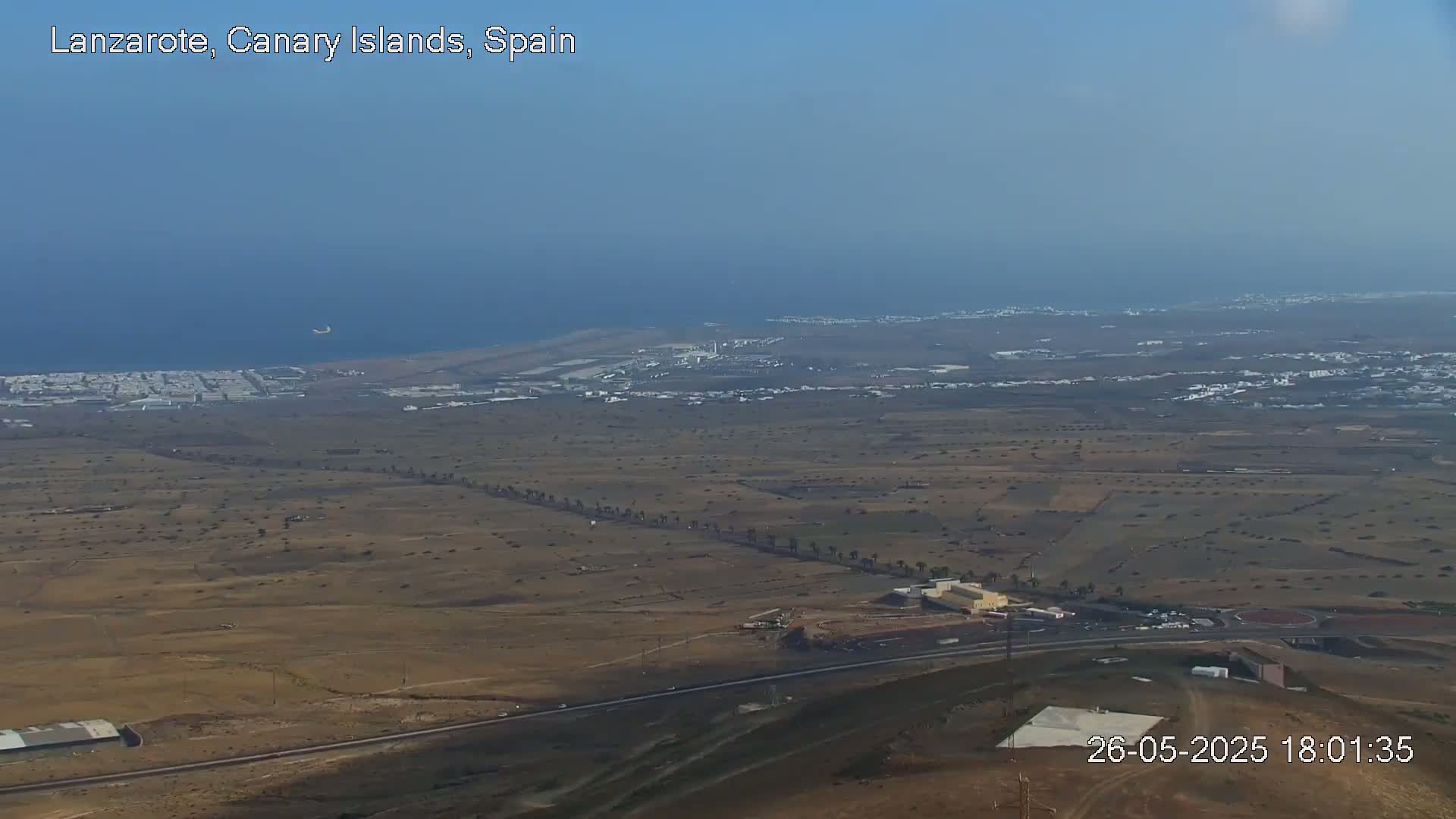 A high-angle, long shot shows a coastal desert landscape with an airport, a town, and a body of water under a clear sky.