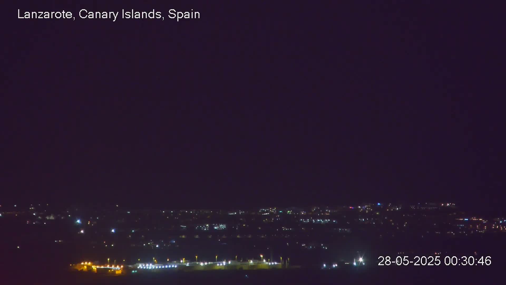 A nighttime long shot shows a city with scattered lights under a dark, clear sky.