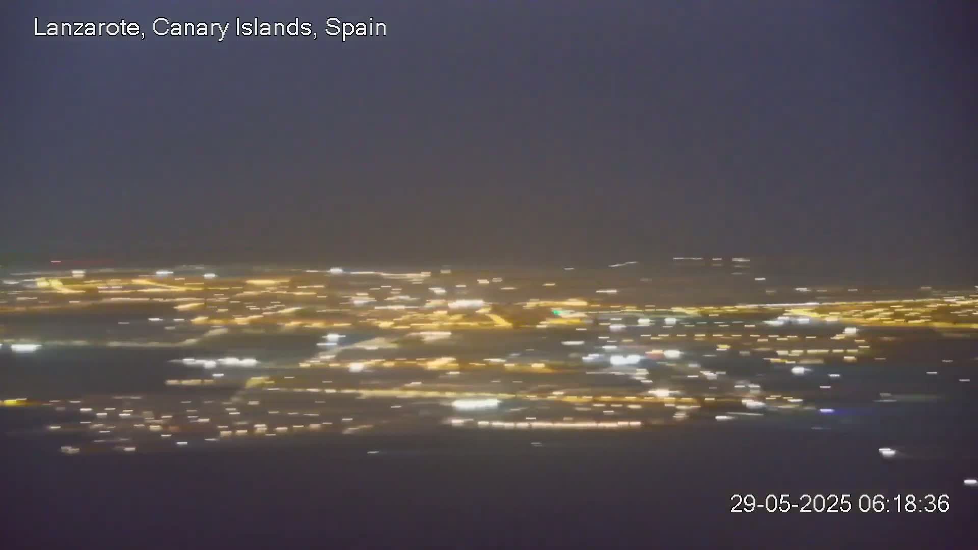 A blurry, nighttime view of a city illuminated by numerous lights under a dark, possibly overcast sky.