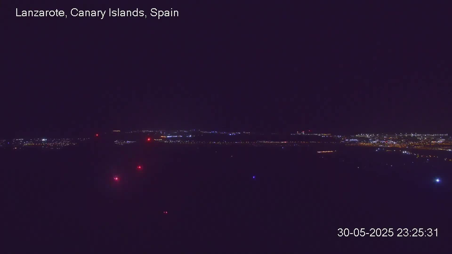 A nighttime, long-distance view of a city's lights scattered across a dark landscape.