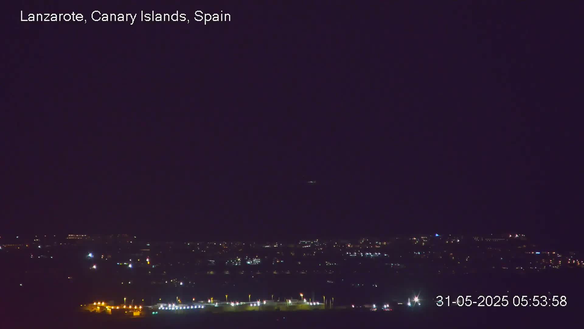 A nighttime long shot shows a dark cityscape with scattered lights under a clear, dark sky.