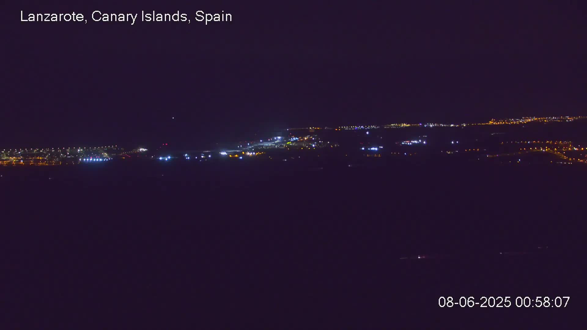 A nighttime long shot shows a distant city illuminated by scattered lights under a clear, dark sky.