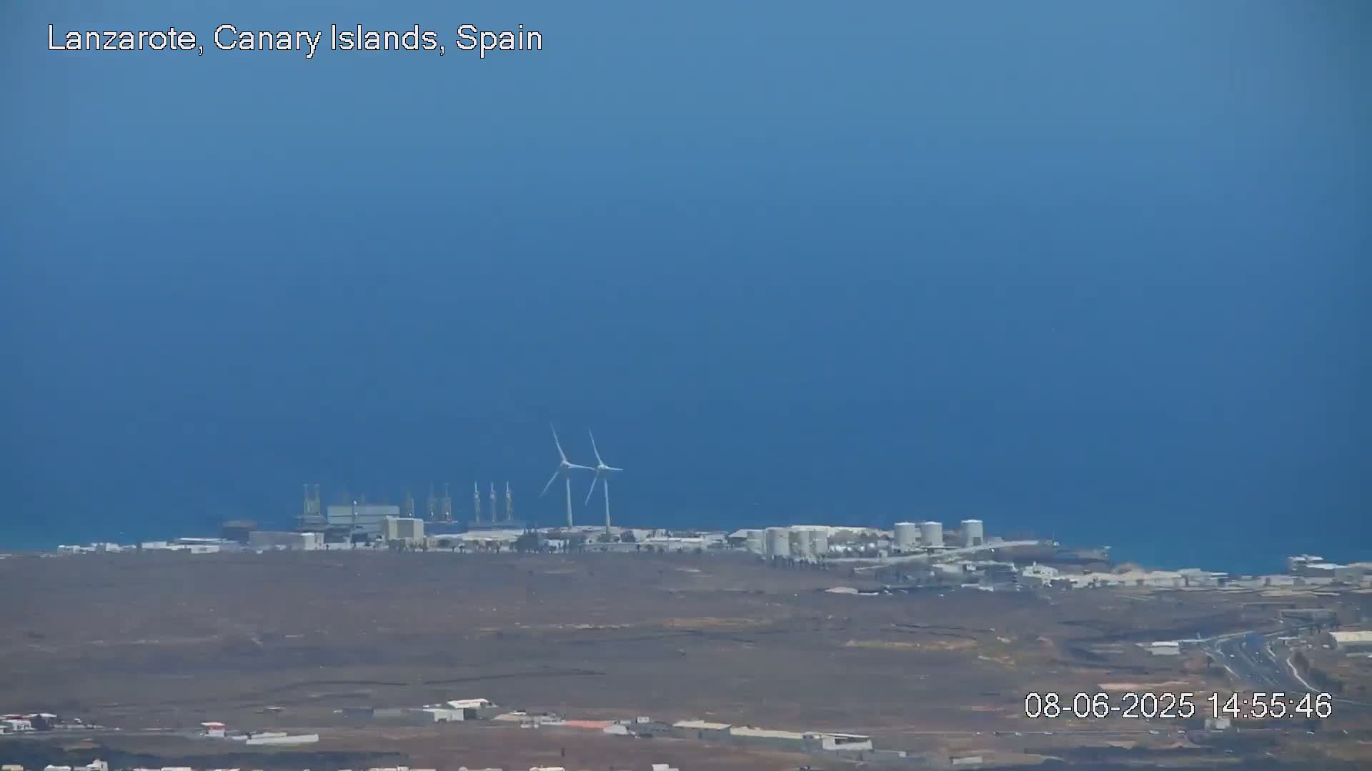 A coastal industrial area with wind turbines is visible under a clear blue sky.
