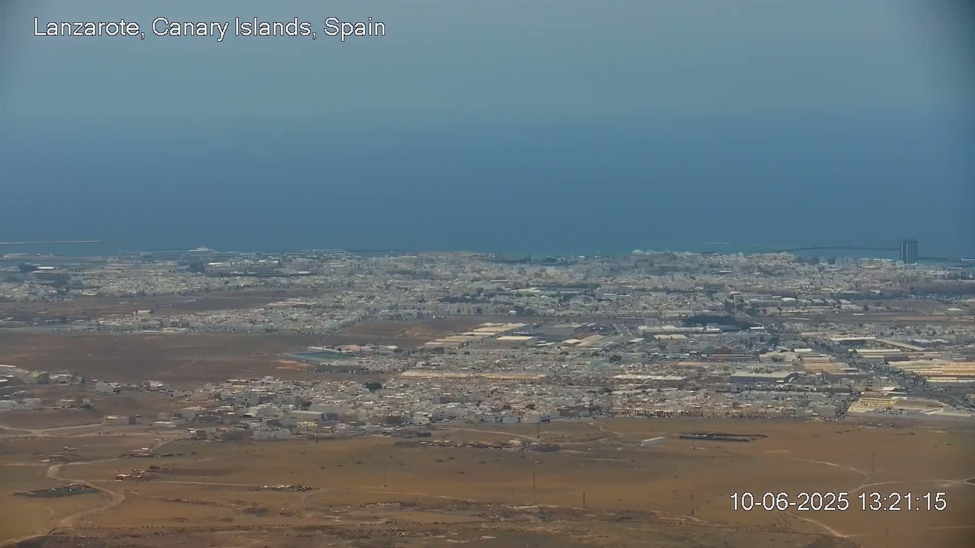 A sprawling city on a dry, brown landscape stretches to a calm blue ocean under a hazy sky.