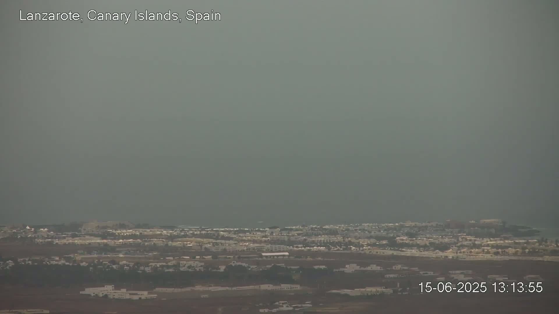 A hazy, overcast view shows a coastal town with low-lying buildings stretching towards a gray ocean.