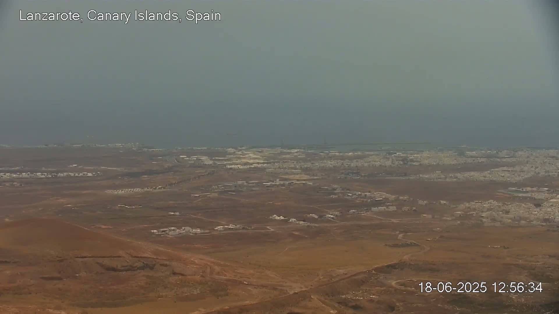 A hazy, long-distance view shows a brown, sparsely populated landscape extending to a gray-blue ocean under an overcast sky.