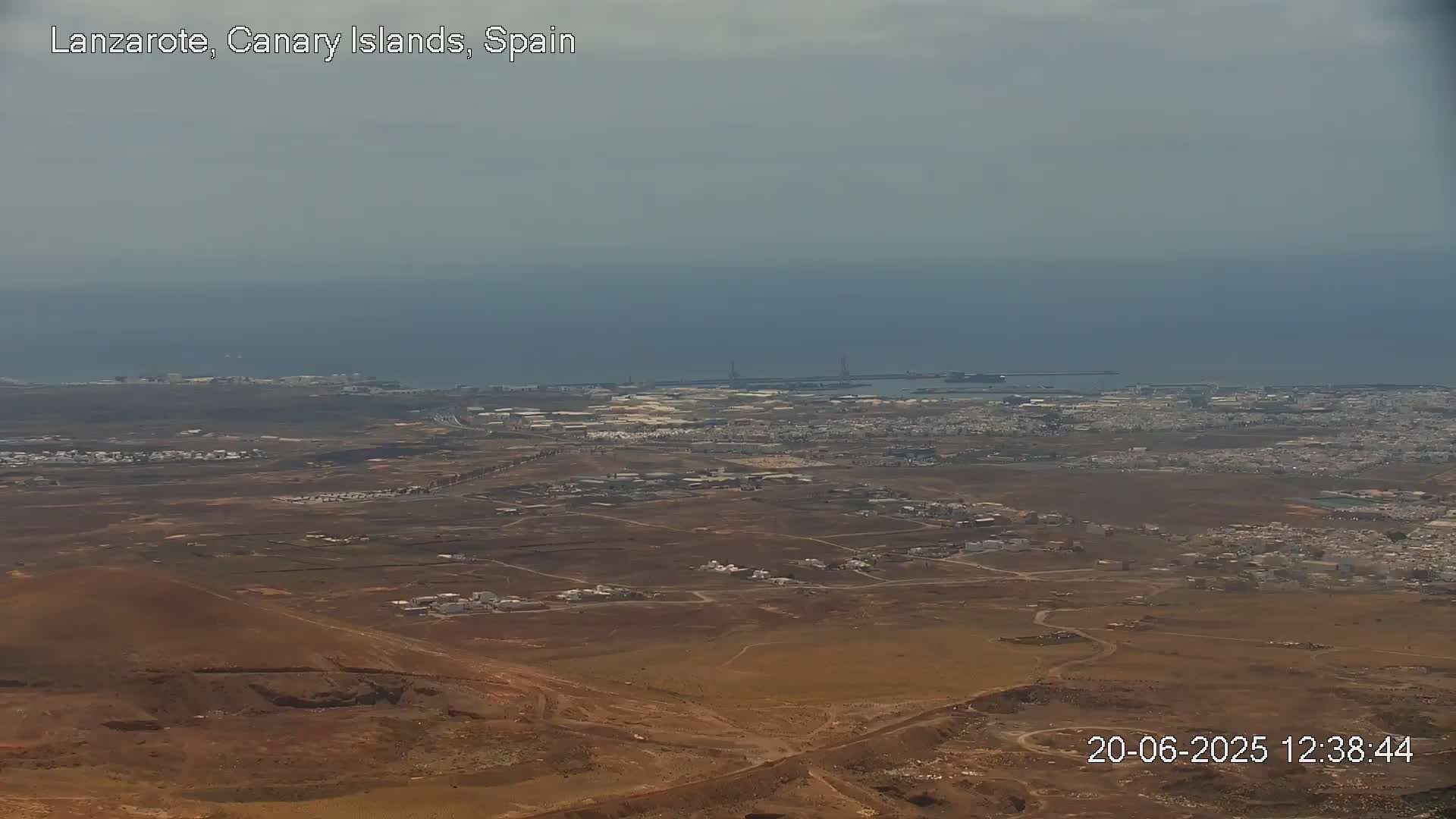 A high-angle, long shot of a coastal town with a hazy sky and calm ocean in the background.