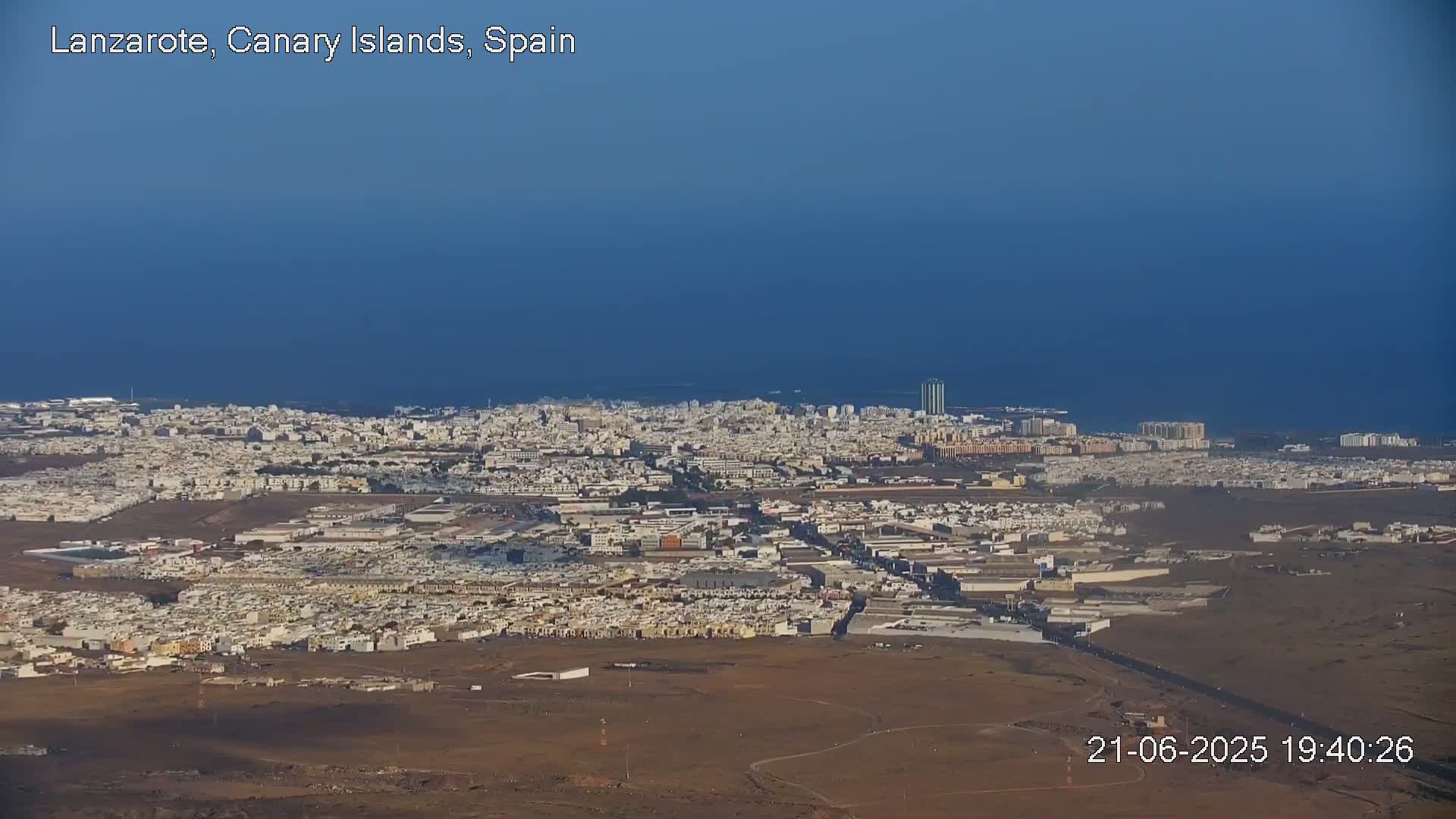 A sprawling city extends to a calm, dark blue ocean under a clear sky.