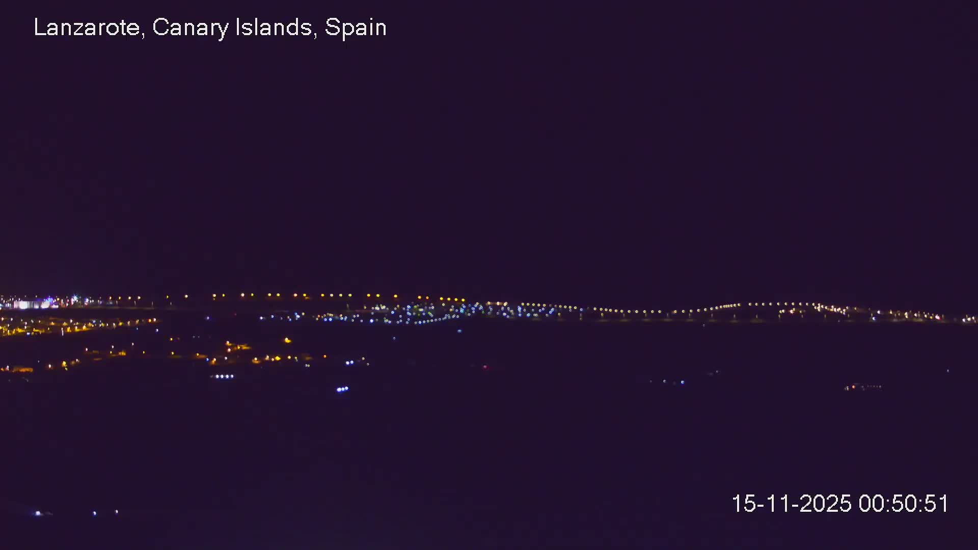 The image displays a panoramic nighttime view of a brightly lit coastline or city under a clear, dark sky.