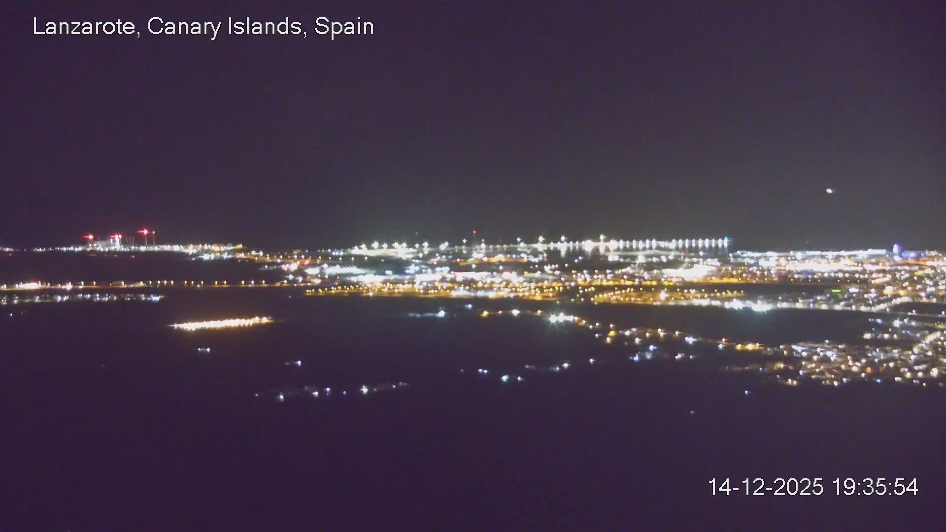 An elevated view reveals a hazy, overcast coastal city stretching towards a calm body of water with streaks of bright light reflecting on its surface under a cloudy morning sky.