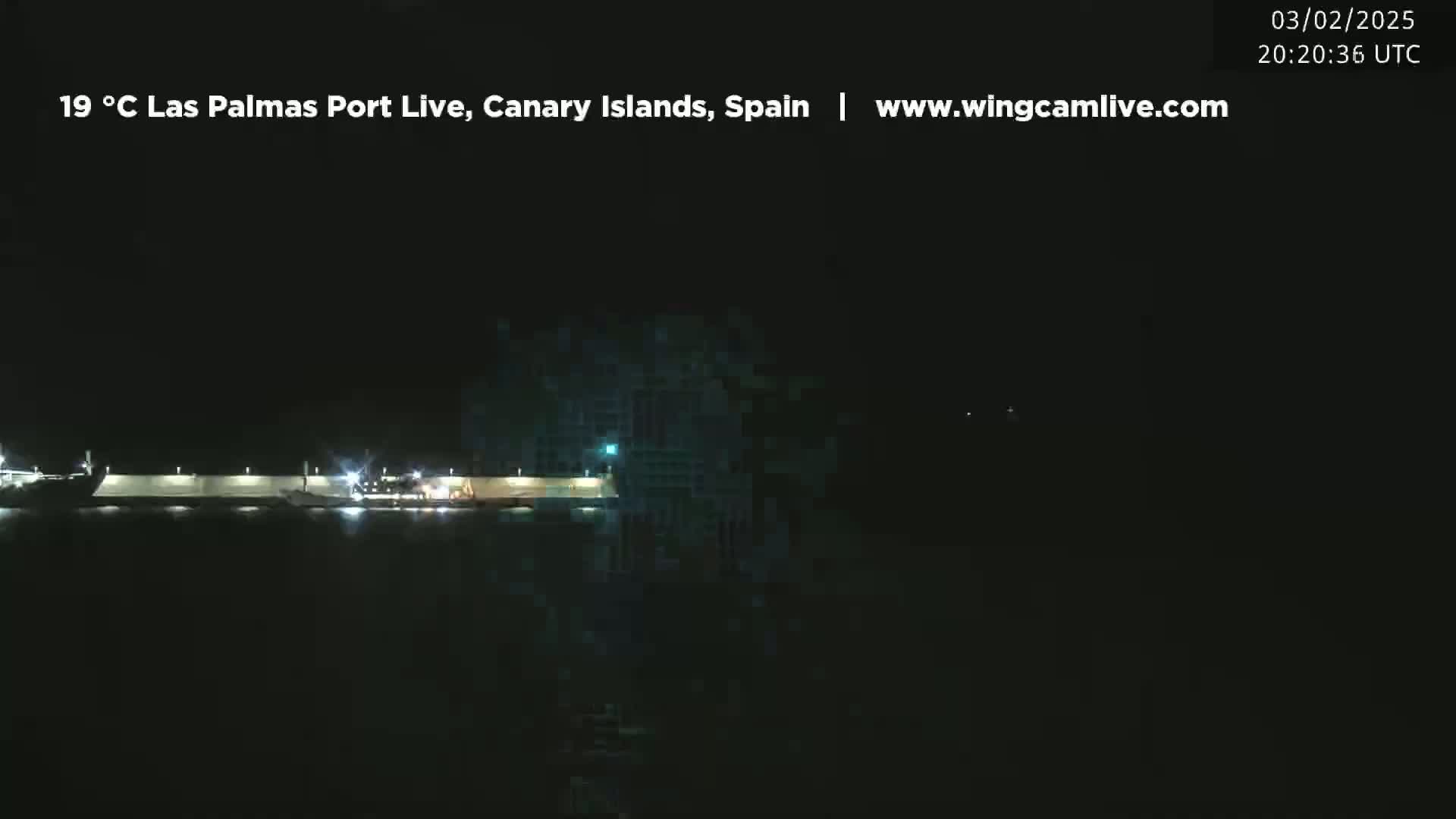 A nighttime, dimly lit view of a port with several structures and vehicles visible along the waterfront.