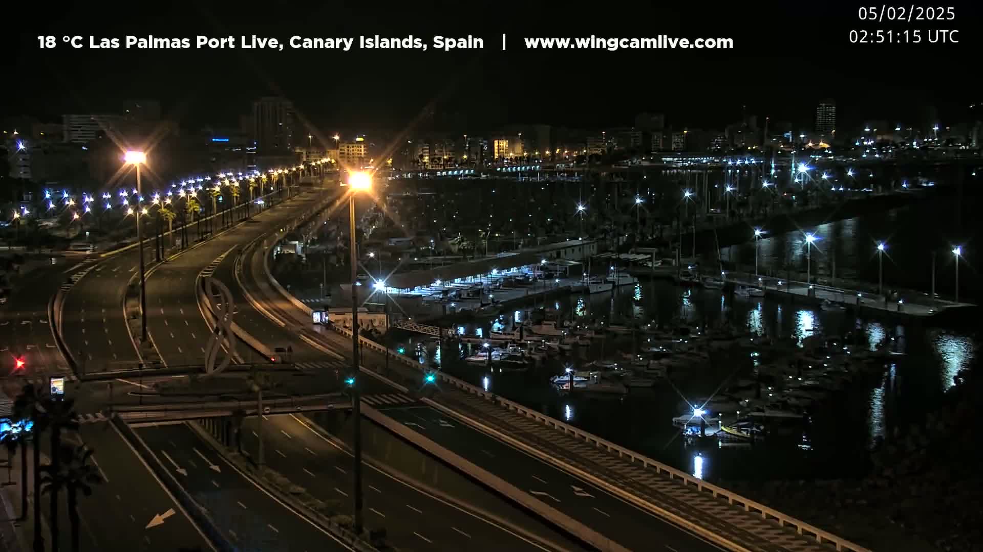 A nighttime aerial view of a harbor filled with boats and a highway lined with streetlights.