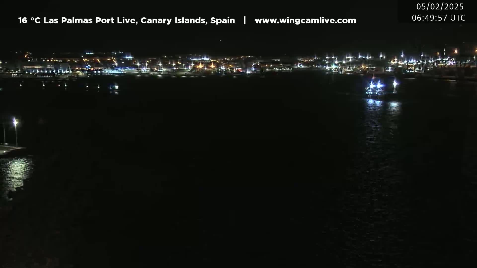 A nighttime view of a brightly lit harbor with a small vessel in the water.