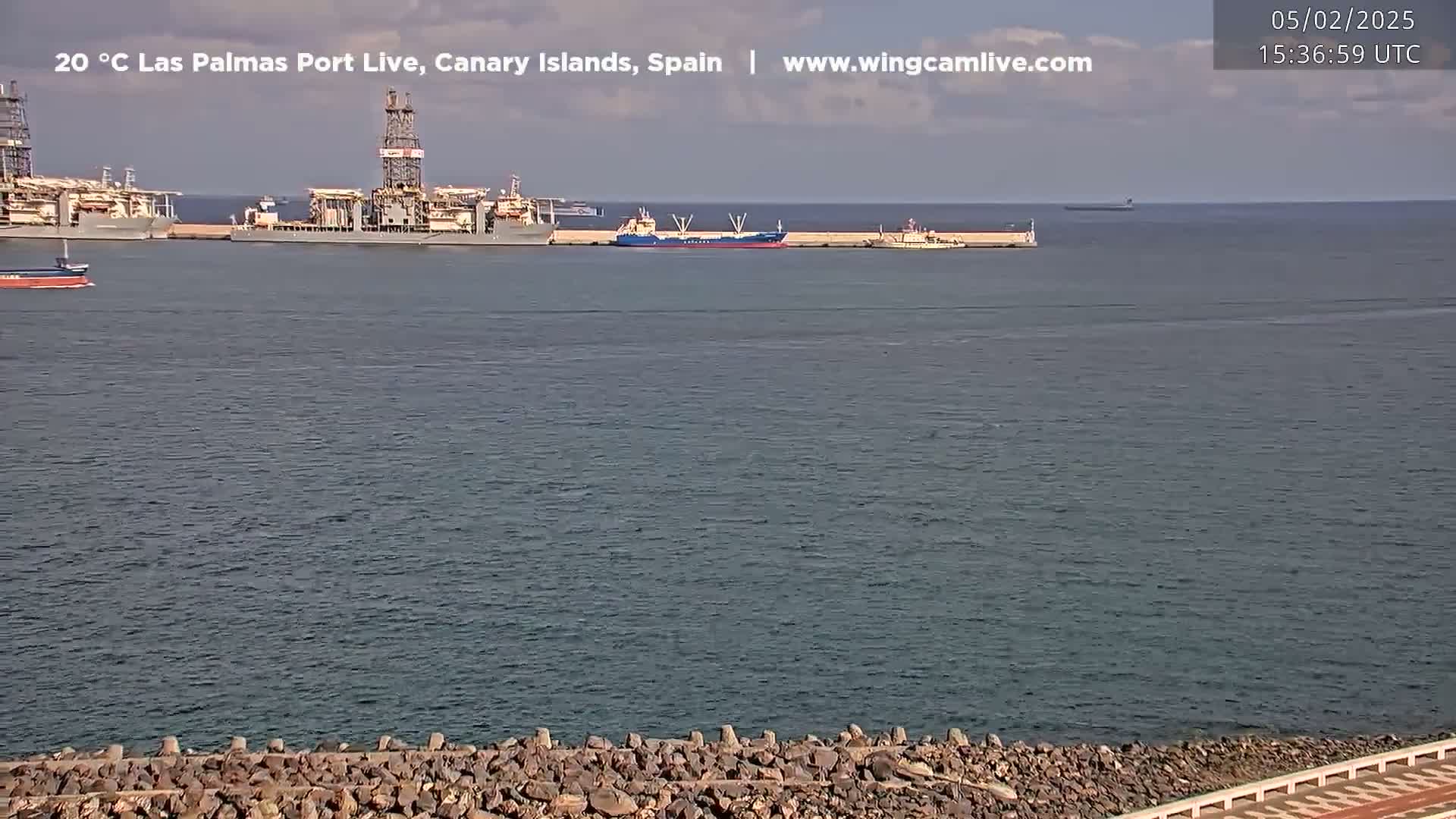 Several ships are docked in a calm harbor on a partly cloudy day.