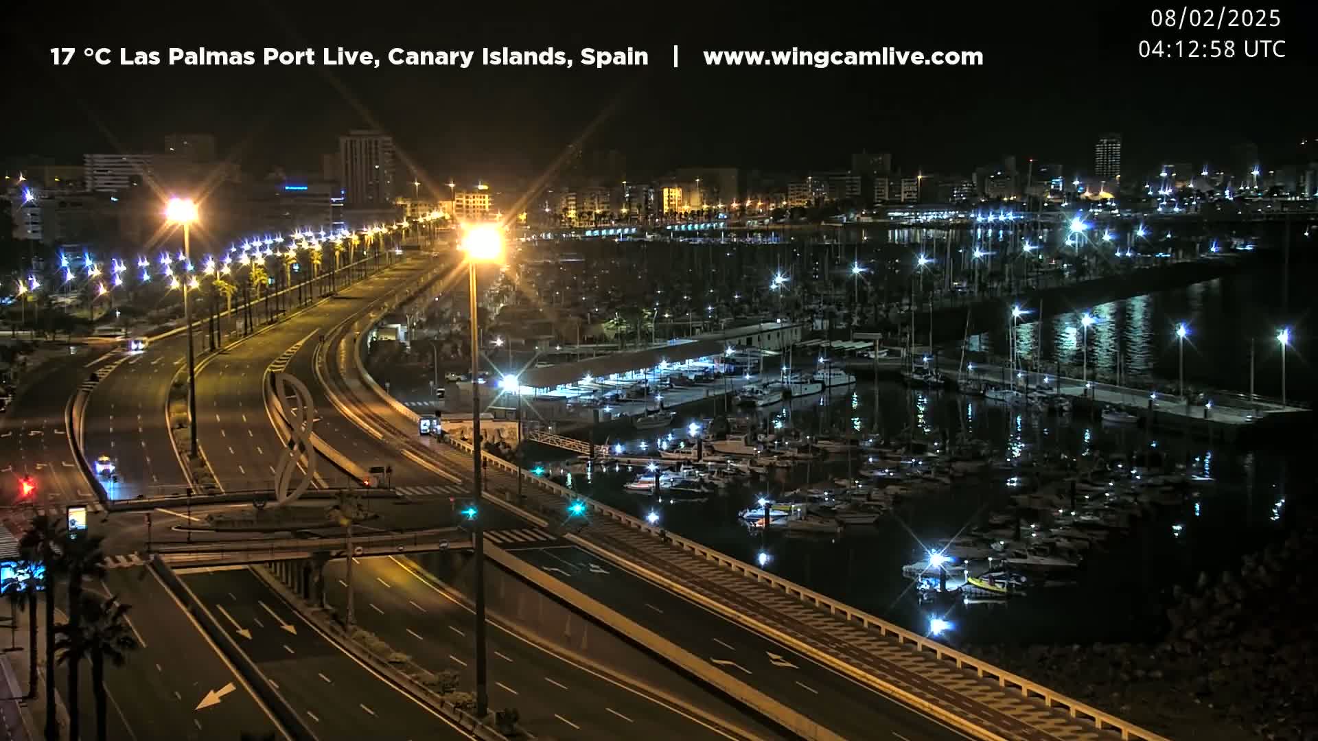 A nighttime view of a marina filled with boats and a well-lit highway beside it.