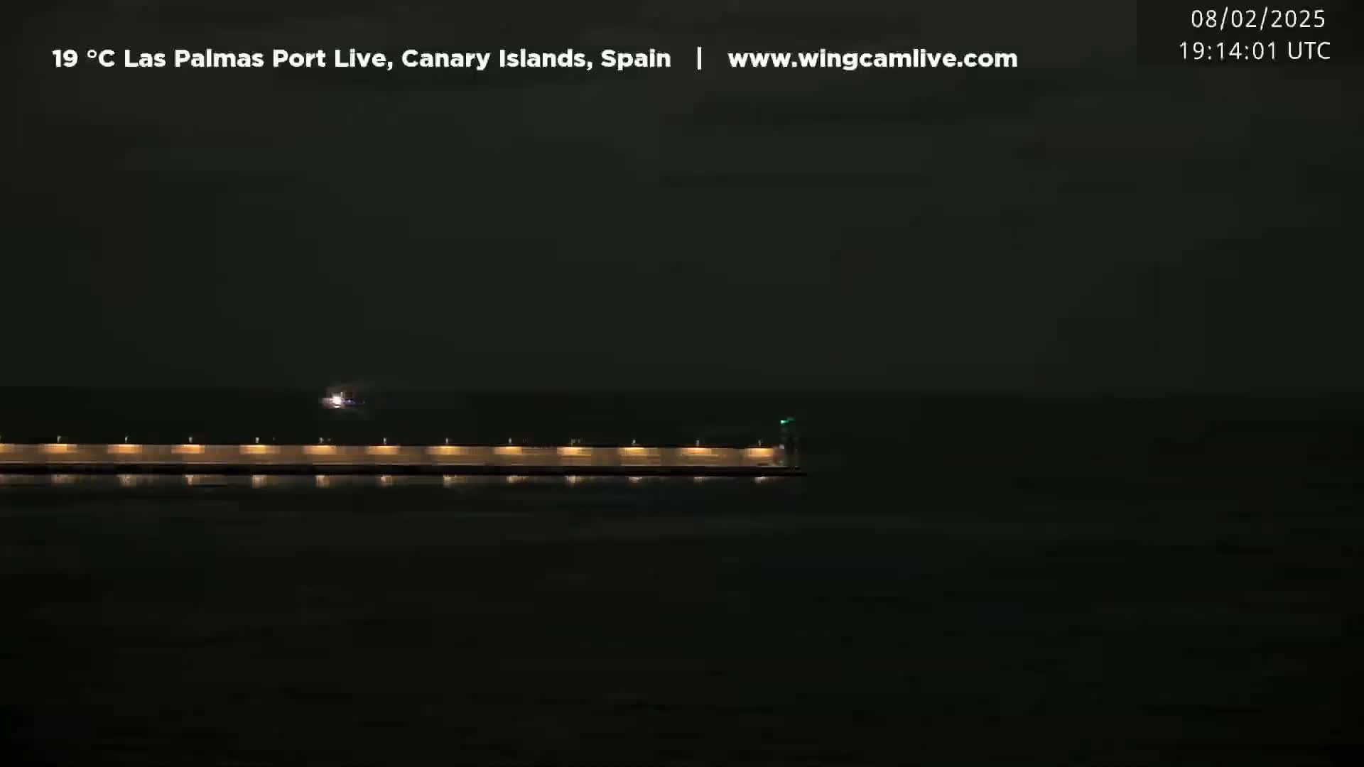 A long, low-lit pier extends into a dark ocean at night.
