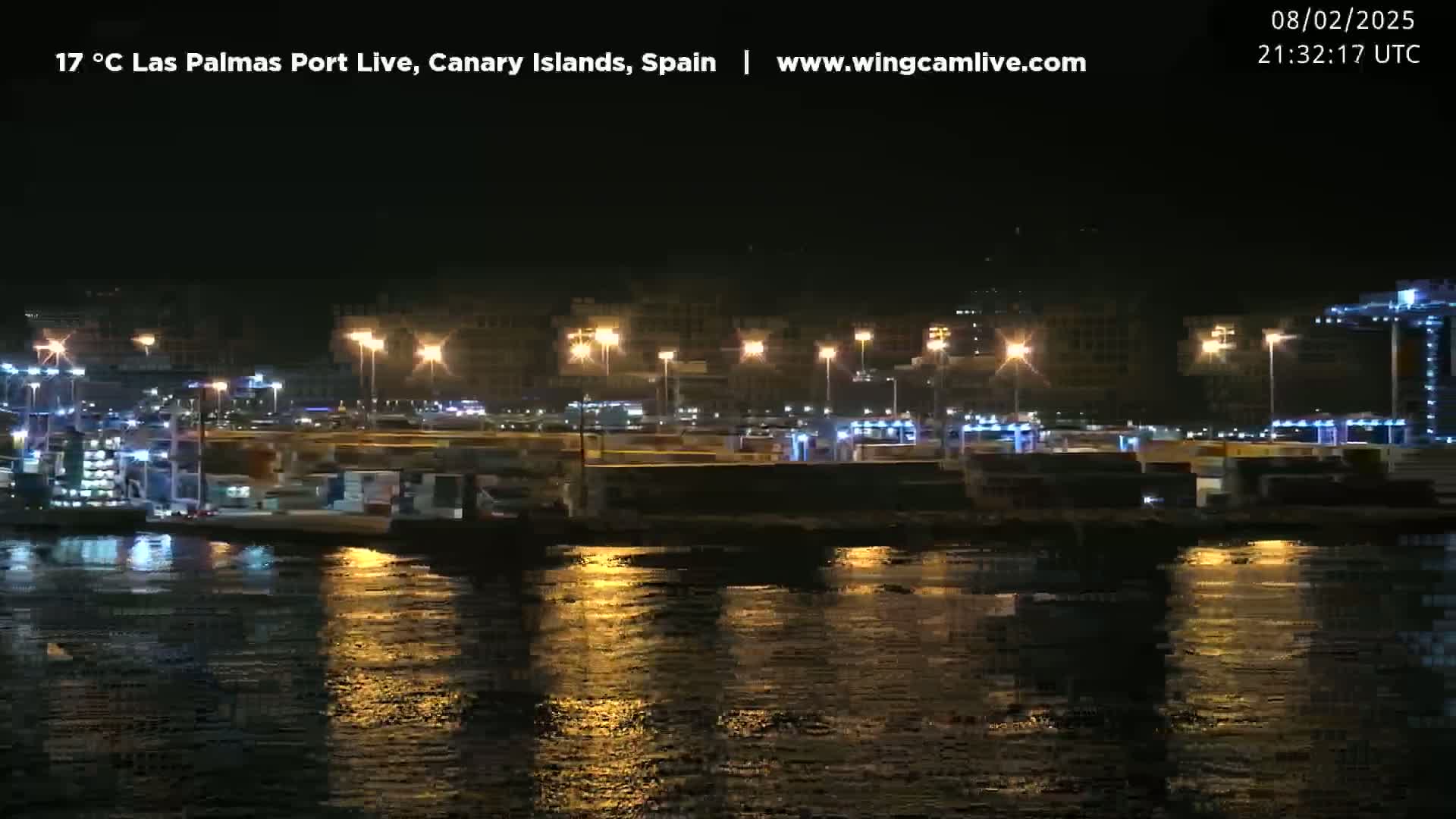 A nighttime view of a brightly lit port with numerous containers and cranes reflected in calm water.